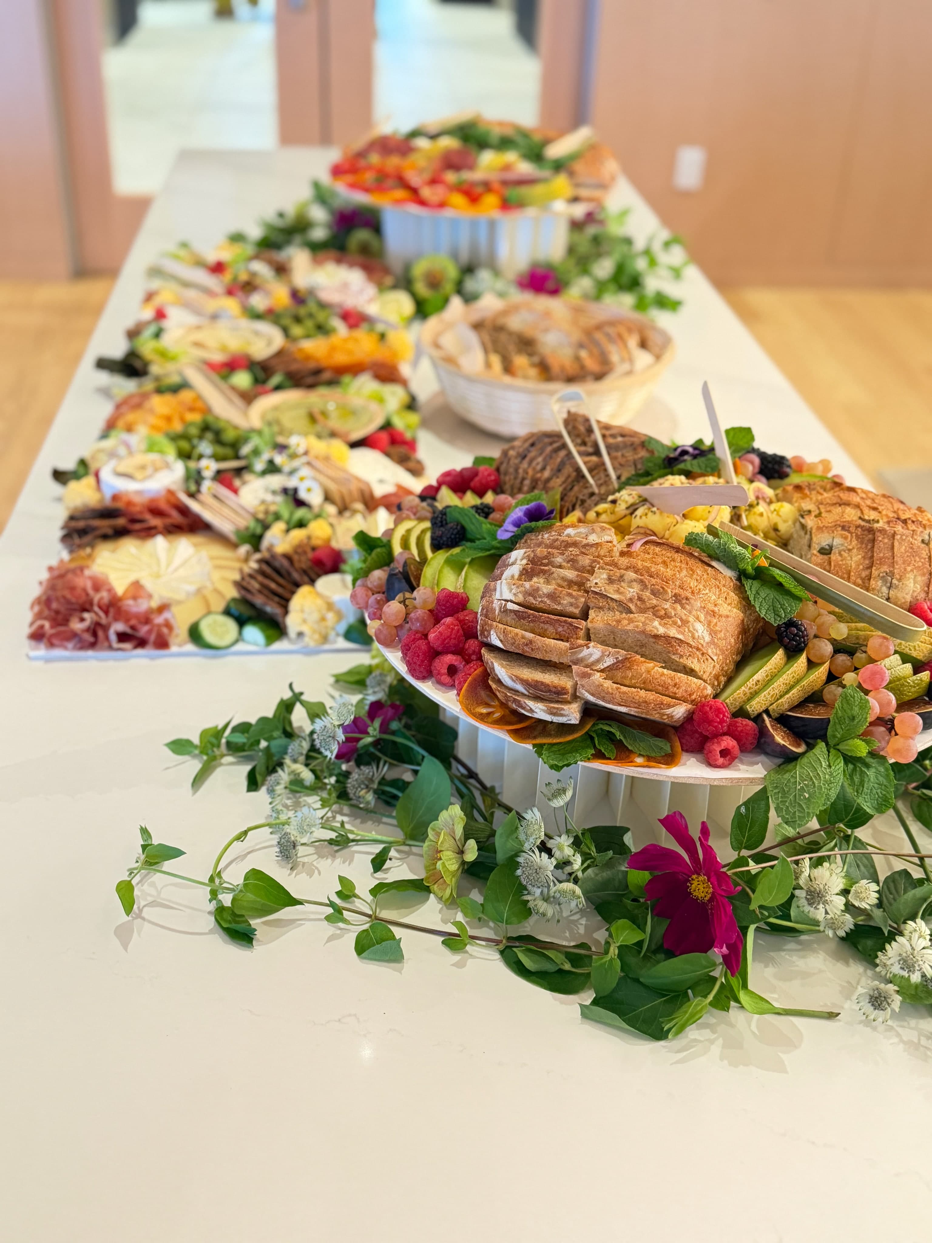 A long grazing table of bread, fruit, charcuterie and flowers laid out for the evening