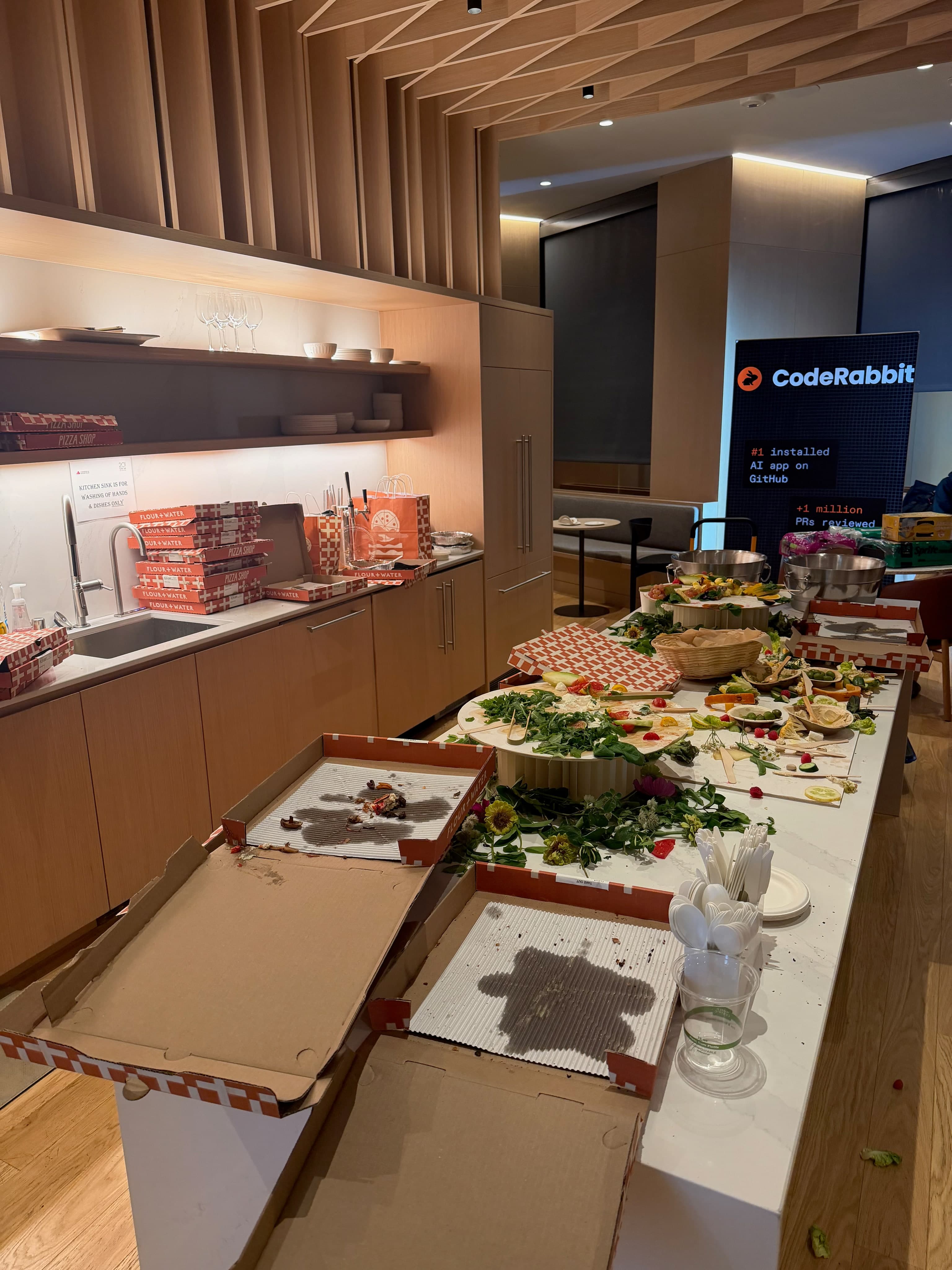 Dinner along the kitchen counter at CodeRabbit, with pizza boxes and a CodeRabbit sign